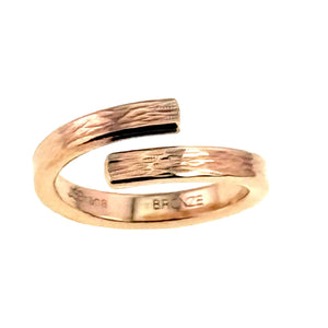 3 of 9: Front view of a handcrafted bronze bypass ring on a white background. The slim open band curves around with two flat ends facing each other, showing a hand applied bark texture across the surface. The warm golden bronze finish has soft polished highlights, and the inside of the band shows a stamped maker mark and bronze metal stamp.