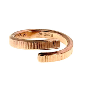 3 of 9: Angled rear view of a polished bronze bypass ring on a white background. The open ring curves around itself with two overlapping textured ends. The inner surface is stamped with the Brana name and BRONZE mark.