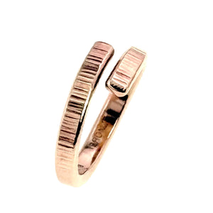 7 of 9: Side view of a 4mm chased bronze bypass ring standing upright on a white background. The open ends face upward and show hand applied vertical texture marks. The polished bronze surface reflects warm rose gold tones.