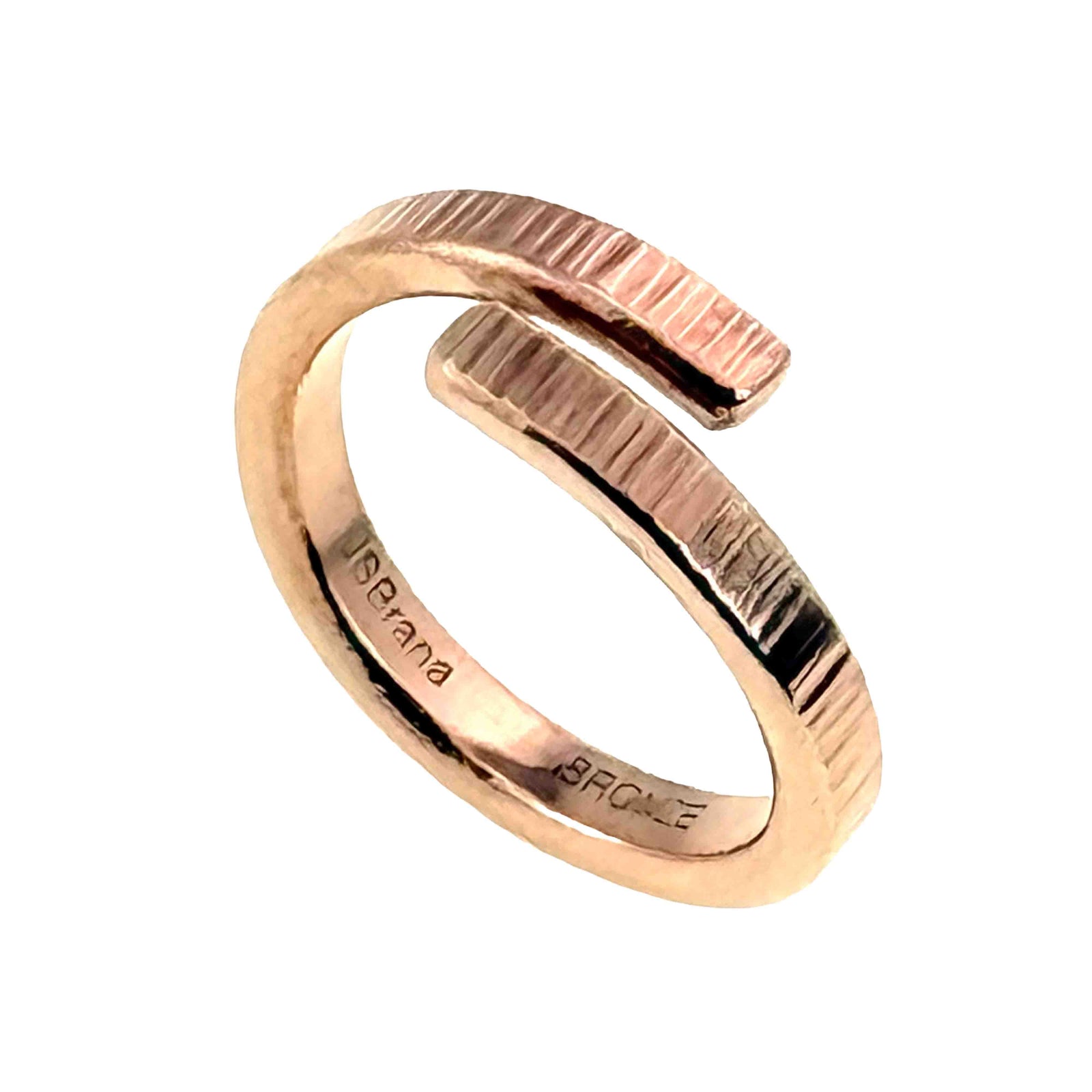 Three quarter view of a polished chased bronze bypass ring on a white background. The wrap style band forms an open circle with two textured ends that pass one another. The inner band includes stamped branding.