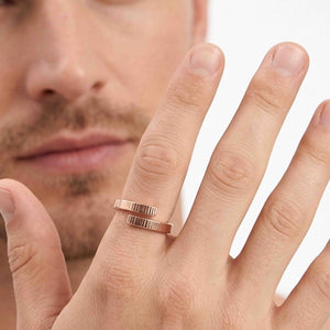 4 of 9: Close view of a man wearing a 4mm chased bronze bypass ring on his finger against a light background. The open wrap design has two parallel textured ends. Part of his face appears softly out of focus behind his hand.