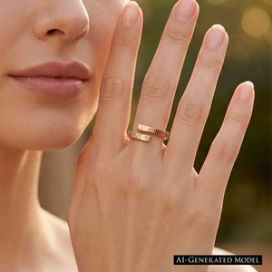 2 of 9: Close view of a woman wearing a slim chased bronze bypass ring on her finger outdoors. The two textured ends wrap around the finger with a small open space between them. Warm sunlight and a softly blurred garden appear in the background.  AI Generated Model.
