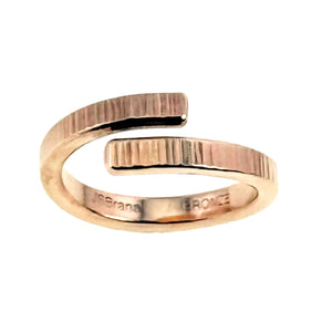 5 of 9: Front view of a polished 4mm chased bronze bypass ring on a white background. The open wrap design has two flat ends with hand applied vertical texture marks. The inner band shows stamped branding.