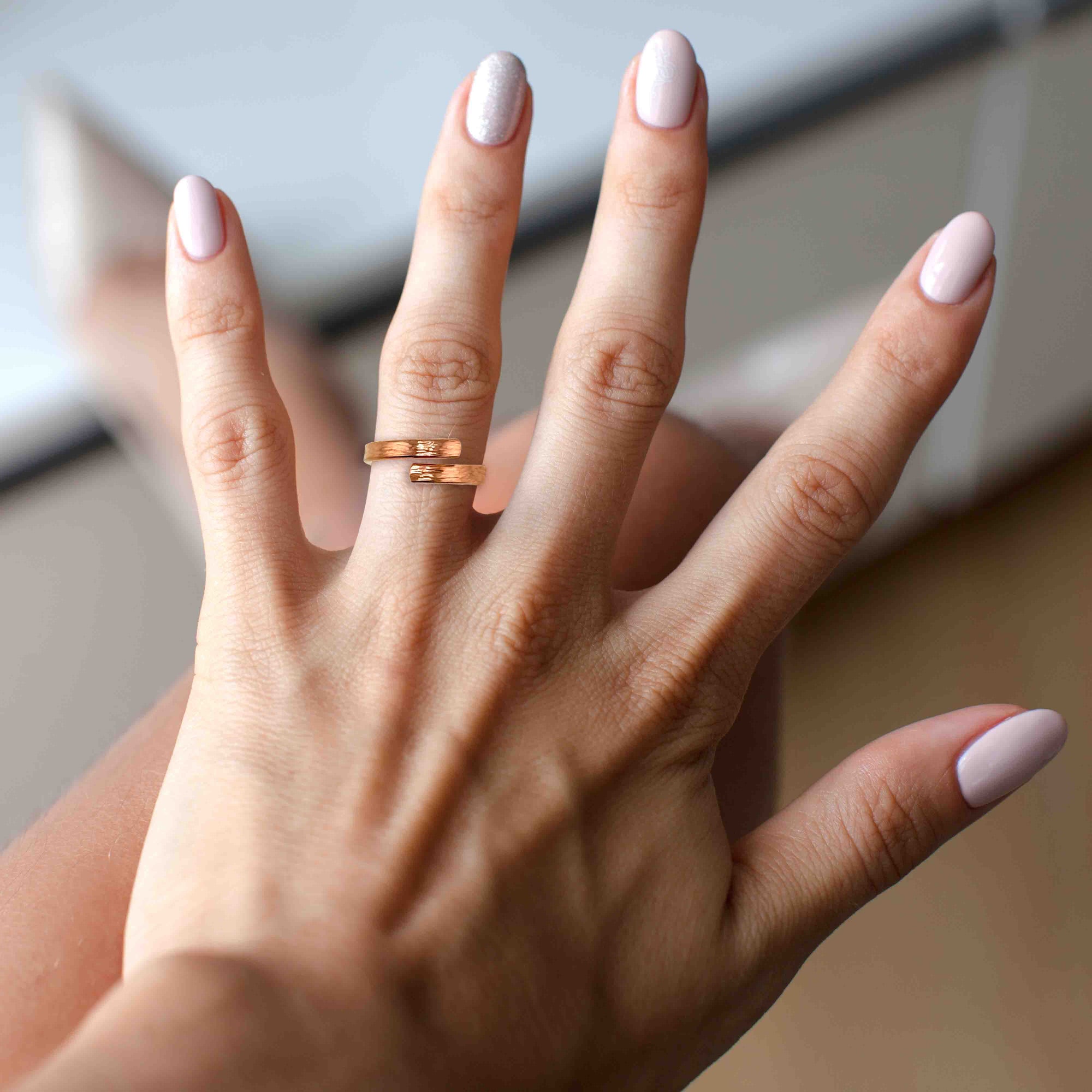 A Woman's Hand with pink nail polish wearing a 4mm Chased Copper Bypass Ring on a neutral background