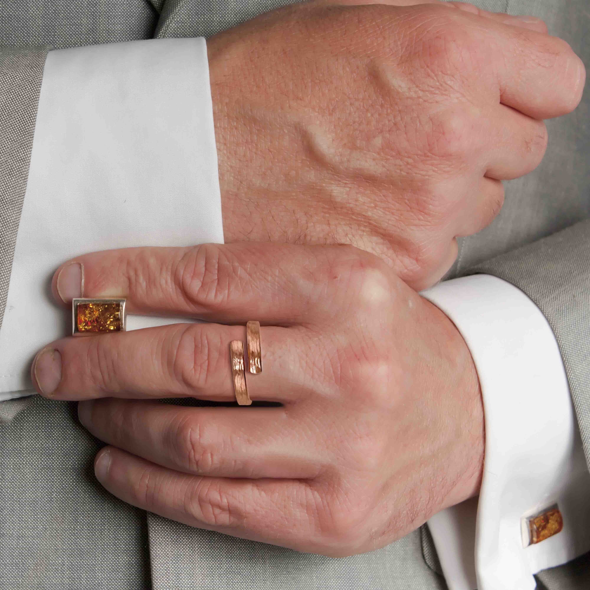 Close-up of a hand wearing a 4mm Chased Copper Bypass Ring with a suit background