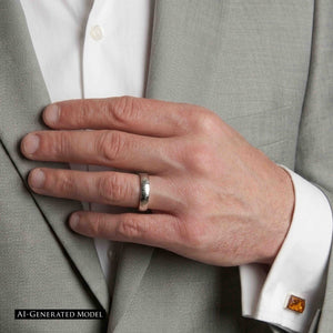 2 of 9: Close view of a man in a light gray suit and white shirt wearing a slim chased stainless steel ring on his ring finger. His hand rests against his jacket near an amber cuff link. The polished textured band stands out against the soft gray fabric. The image includes an AI generated model label.
