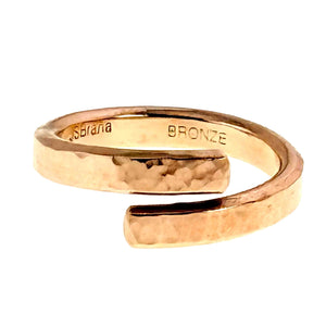 3 of 9: Side view of the hammered bronze bypass ring on a white background. The overlapping open band, polished finish, and interior John S. Brana and BRONZE stamps can be seen.