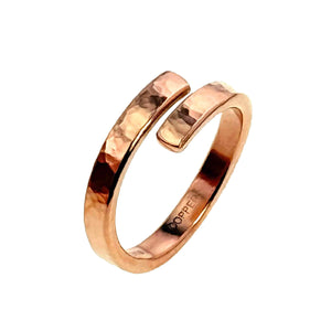 6 of 7: A handcrafted hammered copper bypass ring shown on a white background. The ring features an open-ended wrap design with squared tips that curve past each other. Its surface has a rich, warm reddish tone with a polished finish and a textured, hammered look that reflects light. The inside of the band is stamped with "COPPER," indicating the metal type. The ring's minimalist yet bold style highlights its artisan-made quality.