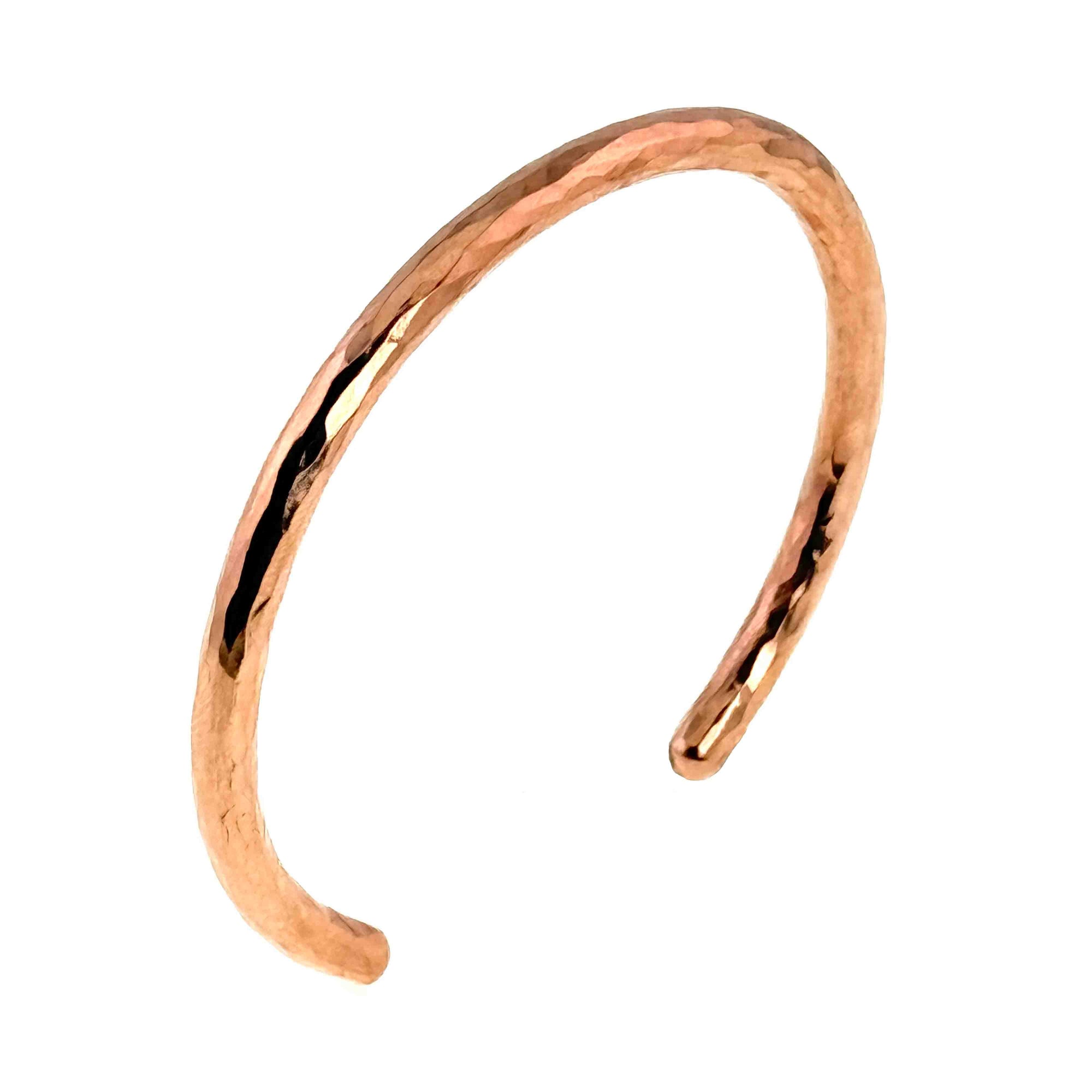 Polished solid 4.75mm Hammered Copper Cuff Bracelet shown on a white background, photographed at an angle to highlight its slim open-band shape. The bracelet features a lightly hammered texture that catches the light across the curved surface, creating bright reflections and subtle dimension. Its narrow profile, rounded ends, and warm copper tone give it a simple, handcrafted look that works well alone or stacked.