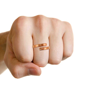 8 of 9: Hand wearing a copper bypass ring with a linen textured finish, shown on a clenched fist against a white background