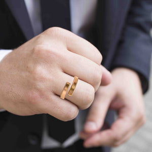 4 of 9: A close-up of a man wearing a 4mm matte bronze bypass ring on his finger. The ring features a brushed finish and an open-ended design with squared tips. He is dressed in a dark suit, with one hand adjusting his jacket or cuff in the background.