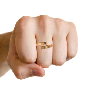 6 of 9: A close-up of a clenched hand wearing a 4mm matte bronze bypass ring. The ring features a brushed finish with an open-ended design and squared tips. The background is white, highlighting the warm bronze tone and minimalist style of the ring.