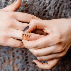 6 of 9: A woman with dark glittery nail polish sliding the 4mm matte copper bypass ring onto her finger while wearing a crocheted top.
