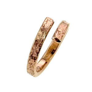 5 of 9: Side view of the bronze bypass ring standing upright on a white background. The open ends curve past one another and show a hand applied textured surface, while the polished inner band reflects warm golden and copper tones.
