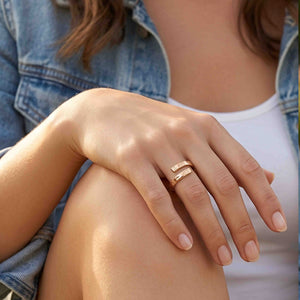 8 of 9: Close view of a woman wearing the bronze bypass ring while dressed in a denim jacket and white top. Her hand rests casually on her knee, showing how the warm polished ring and textured open ends suit relaxed everyday clothing.
