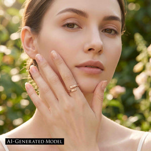 2 of 9: Close view of a woman wearing a warm bronze bypass ring on her finger while resting her hand against her face. Soft natural light and blurred green foliage highlight the ring’s open shape, polished finish, and textured ends.  AI Generated Model.