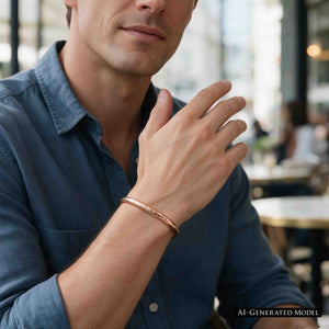 7 of 10: AI generated male model wearing a polished 5.25mm hammered solid bronze cuff bracelet by John S. Brana with a casual blue button down shirt. The close up emphasizes the bracelet's slim profile, rich golden bronze coloring, and reflective hammered finish. The simple open cuff design illustrates how handmade bronze jewelry can be worn as an everyday men's fashion accessory.
