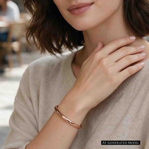 4 of 10: AI generated female model wearing a polished 5.25mm hammered bronze cuff bracelet by John S. Brana with a soft beige sweater. The close up highlights the bracelet's warm golden bronze color, hand hammered texture, and slender curved design. Her hand rests near her shoulder, illustrating how this handmade solid bronze bracelet complements relaxed everyday fashion.