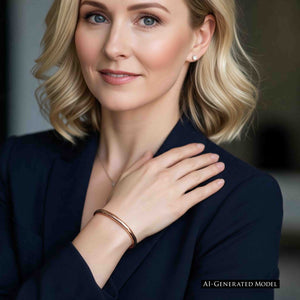 9 of 10: AI generated blonde female model wearing a 5.25mm hammered solid bronze cuff bracelet by John S. Brana with a tailored navy blue blazer. The polished bronze bracelet features a slender profile and reflective hand hammered texture that contrasts beautifully with the dark fabric. The image illustrates how handmade bronze jewelry adds warmth and understated sophistication to professional attire.
