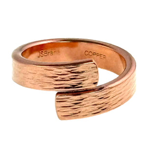 7 of 9: Studio close up of the 5.5mm bark copper bypass ring on a white background, showing polished solid copper, rounded edges, overlapping bypass ends, bark textured surface, and stamped maker marks inside the band.