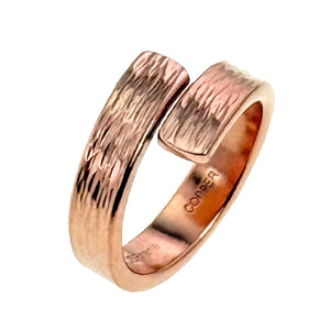 3 of 9: Angled studio view of the bark copper bypass ring standing upright on a white background, highlighting the open wrap design, polished copper shine, textured outer surface, and smooth inner band with stamped markings.