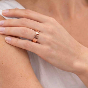 8 of 9: Close view of a woman wearing a polished 5.5mm bark copper cuff ring with a white top, showing the open ends, hand textured surface, warm copper color, and comfortable medium width on the finger.