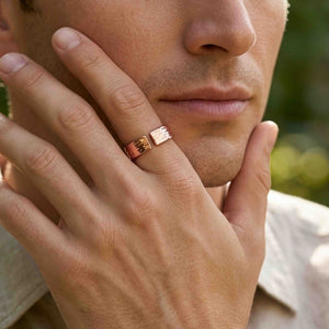 2 of 9: Close view of a man wearing a polished bark textured copper cuff ring on his finger while resting his hand against his face outdoors, showing the ring’s open design, warm copper tone, and unisex styling.