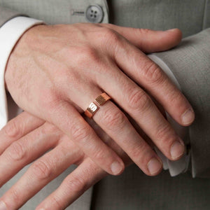 6 of 9: Man wearing a 5.5mm bark copper cuff ring with a light gray suit and white shirt, showing the open textured ends and polished copper finish as his hands rest together in a formal setting.