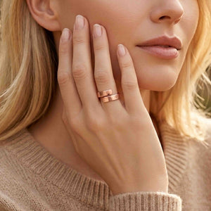 2 of 8: Close view of a woman wearing a 5.5mm chased copper bypass ring while resting her hand against her face. Warm sunlight highlights the polished copper surface, overlapping open ends, and fine hand applied texture.