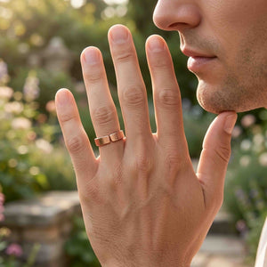 3 of 8: Close up lifestyle photo of a man wearing a 5.5mm chased copper cuff ring on his finger outdoors. The open cuff design and polished copper surface are visible against a softly blurred garden background.