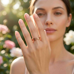 2 of 8: Outdoor lifestyle photo of a woman wearing a 5.5mm chased copper cuff ring. Her raised hand shows the open cuff shape and hand applied vertical texture against a softly blurred garden with flowers.