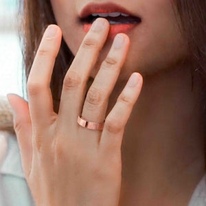 6 of 8: Close up lifestyle photo of a woman wearing a 5.5mm chased copper cuff ring on her finger. The polished copper band and open cuff ends are clearly visible as her hand rests near her face.