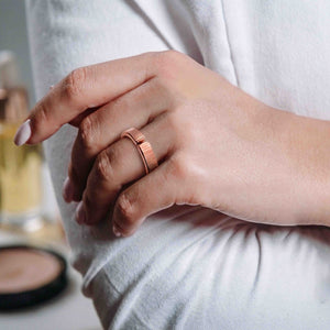 7 of 8: Close up lifestyle photo of a woman wearing a 5.5mm chased copper cuff ring while dressed in a light gray robe. The ring’s warm copper tone, open cuff gap, and chased surface are visible on her finger.