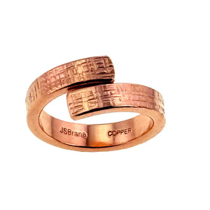 2 of 8: Angled front view of a solid copper bypass ring with a linen textured finish. The handcrafted unisex ring shows its open wrap design and smooth polished interior stamped with John S. Brana branding on a white background.