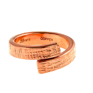 6 of 8: Close up front view of a handcrafted 5.5mm linen copper bypass ring made from raw solid copper. The ring features a hand applied linen texture with overlapping open ends and a warm polished copper glow on a white background.