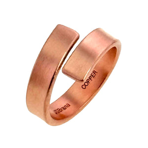 7 of 9: Angled product view of a matte copper bypass ring, showing the overlapping open design, flat band, rounded edges, brushed copper finish, and interior copper stamp.