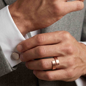 6 of 9: Close up of a matte copper bypass ring worn on a man’s finger while adjusting a white shirt cuff with a gray suit jacket, showing warm copper color and clean modern styling.