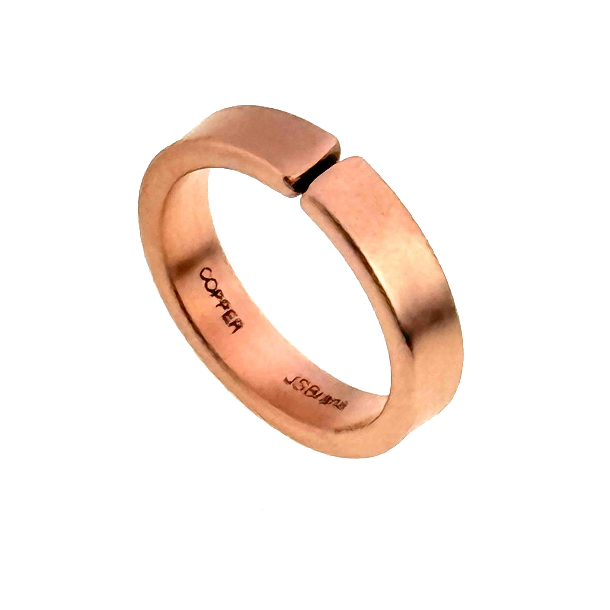 Matte finish solid copper cuff ring shown on a light gray background, photographed at an angle to reveal its open adjustable band and clean modern shape. The ring has a smooth, softly brushed surface with rounded edges and a warm rose-copper tone. Inside the band, the stamped words “COPPER” and “JSBrana” are visible, highlighting the handcrafted maker mark and metal type.