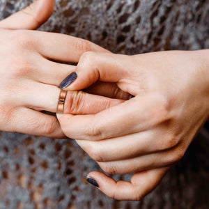 5 of 10: Close-up of two hands with a 5.5mm Matte Copper Cuff Ring on a textured brown background