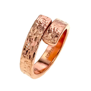 5 of 9: Angled studio photo of a 5.5mm texturized copper bypass ring, highlighting the raised hand chased texture, warm polished copper finish, open bypass design, and stamped copper interior.