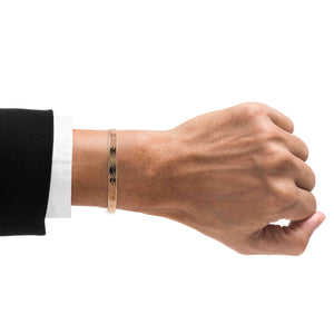 2 of 9: A close-up image of a man's wrist wearing a 5mm wide handcrafted bronze cuff bracelet with a subtle bark texture. The bracelet has a warm, natural bronze tone and a polished finish. The man is dressed in a black suit jacket and white shirt, highlighting the bracelet's refined yet earthy style.