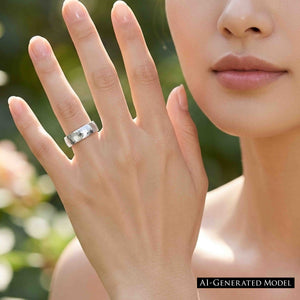 8 of 8: Close view of a woman holding her hand near her face while wearing a polished 5mm chased stainless steel comfort fit ring on her ring finger. The reflective silver tone band stands out against a softly blurred green outdoor background.  AI Generated Model.