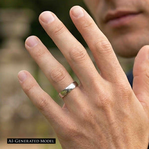 2 of 8: Close view of a man wearing a polished 5mm chased stainless steel comfort fit ring on his ring finger. The silver tone band catches the light while his hand is raised near his face against a softly blurred outdoor background.  AI Generated Model.