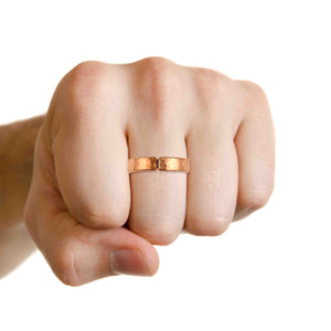 6 of 9: Male hand in a fist pose, wearing the 5mm Hammered Copper Cuff Ring on the middle finger, highlighting the ring’s shine and texture.