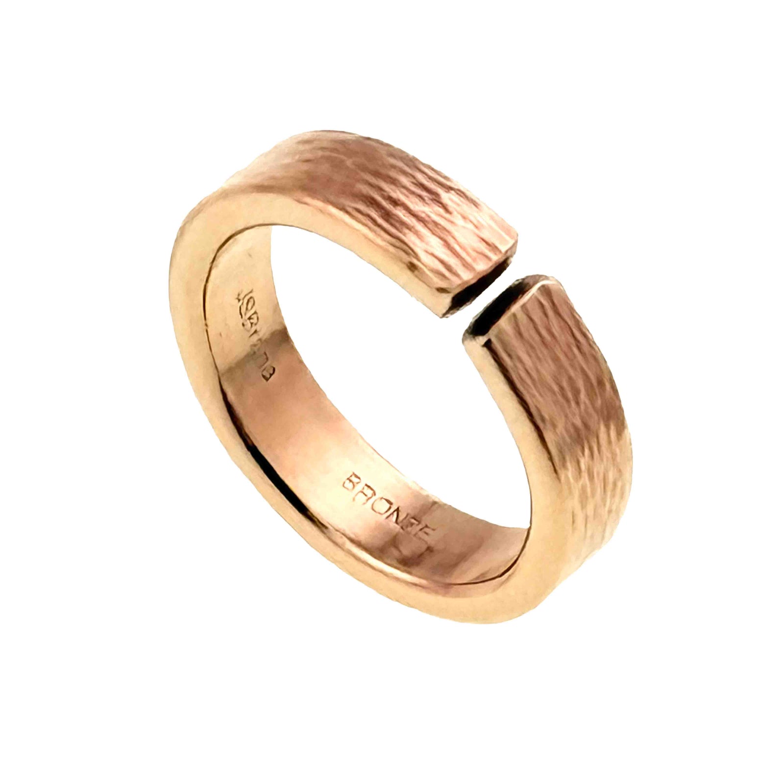 Close-up image of a 6mm wide open cuff ring in solid bronze with a hand-applied bark texture. The ring has a slightly curved band with a narrow gap at the top, showing its adjustable cuff style. The outer surface features an organic, tree bark-inspired pattern, while the inner band is smooth and polished, stamped “BRONZE.” The warm golden-brown metal is shown against a light gray background.