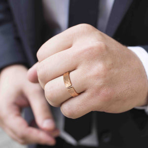 2 of 9: Close-up photo of a man’s hand wearing a 6mm solid bronze cuff ring with a bark-textured finish. The open band design shows a small gap at the top, highlighting the adjustable style. The warm coppery bronze contrasts with the wearer’s light skin tone. The background is softly blurred, with the person dressed in a dark suit jacket and white shirt, giving the ring a modern, unisex look.