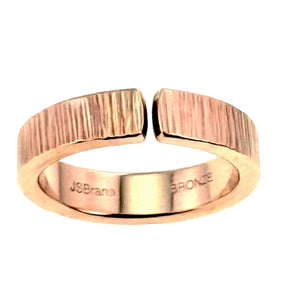 5 of 9: Angled overhead view of a 6mm chased bronze cuff ring on a white background. The open front gap, polished inner surface, rounded band edges, hand applied vertical texture, and interior John S. Brana bronze stamp are visible.