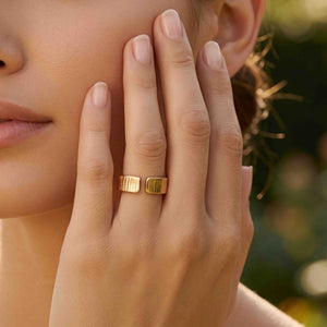 8 of 9: Woman wearing a 6mm chased bronze cuff ring while resting her hand against her cheek outdoors. Warm natural light brings out the polished bronze color, open cuff design, and hand applied vertical texture against a softly blurred garden background.