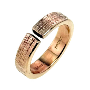 7 of 9: Angled view of the 6mm linen textured bronze cuff ring on a white background, showing the open bypass style, polished warm bronze finish, flat textured ends, smooth inner band, and maker stamps inside.