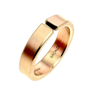 9 of 10: Angled side view of a handmade 6mm matte bronze cuff ring standing upright on a white background, showing the open cuff design, rounded outer edge, smooth interior, and BRONZE stamp.